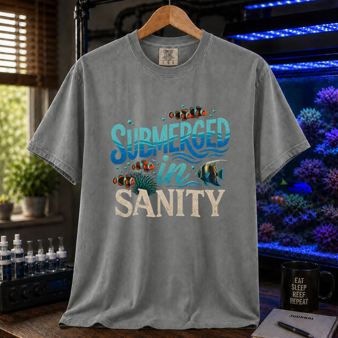 Saltwater aquarium graphic t-shirt design featuring wavy blue typography reading Submerged In Sanity with clownfish and coral artwork on a grey tee