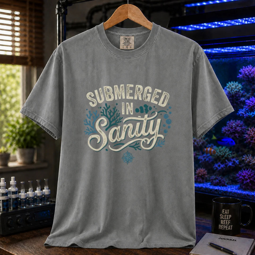 Saltwater aquarium graphic t-shirt featuring distressed cream and teal typography reading Submerged In Sanity with coral and bubble accents printed on a grey tee displayed in a reef room setting