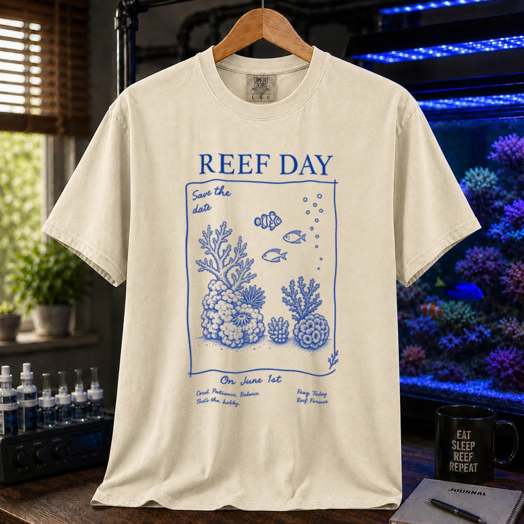 Saltwater aquarium graphic t-shirt featuring blue line-art typography and illustrations reading Reef Day Save The Date On June 1st with coral and fish graphics printed on a beige, cream, ivory tee displayed in a reef room setting