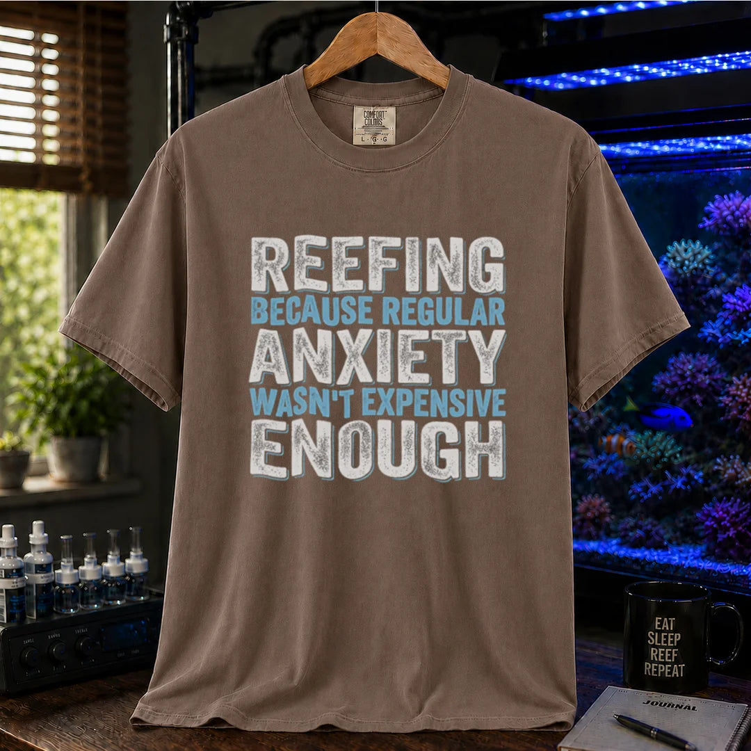 Saltwater aquarium graphic t-shirt featuring distressed block typography in white and light blue reading Reefing Because Regular Anxiety Wasn't Expensive Enough on a brown shirt