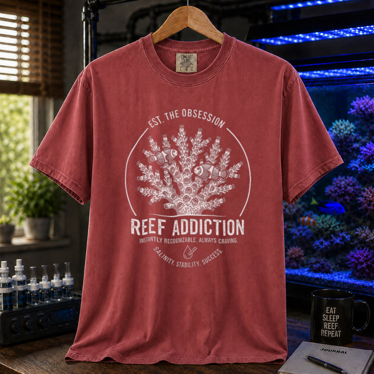Broke Reefers saltwater aquarium graphic t-shirt featuring a circular emblem with coral, clownfish, and text: EST. THE OBSESSION, REEF ADDICTION, INSTANTLY RECOGNIZABLE. ALWAYS CRAVING, SALINITY. STABILITY. SUCCESS., maroon crew neck tee