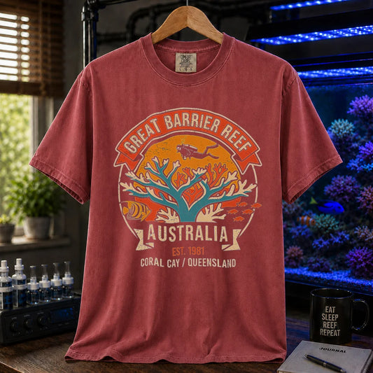 Saltwater aquarium graphic t-shirt featuring a retro colorful emblem of a scuba diver over a coral reef and text: GREAT BARRIER REEF, AUSTRALIA, EST. 1981, CORAL CAY / QUEENSLAND, maroon crew neck tee