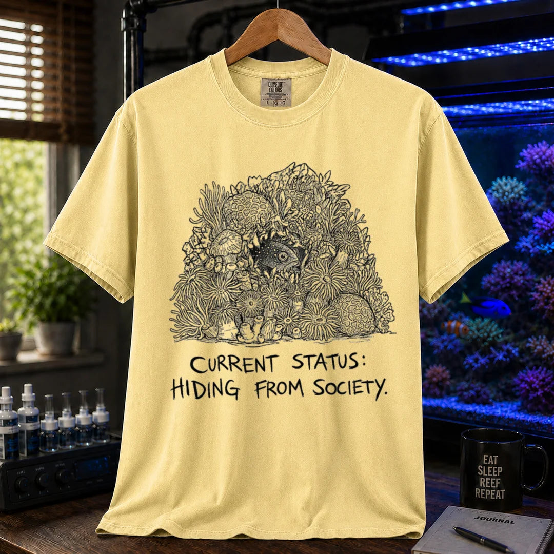 Saltwater aquarium graphic t-shirt on a pure solid white fabric background featuring an ink illustration of a fish hiding in coral and text: CURRENT STATUS: HIDING FROM SOCIETY, yellow crew neck tee