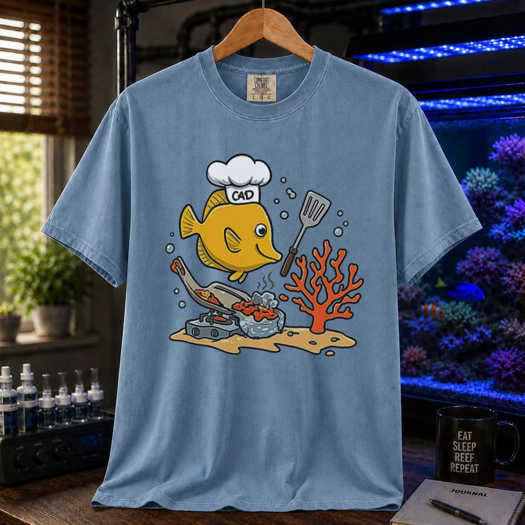 Saltwater aquarium graphic t-shirt featuring a yellow Tang wearing a chef hat and cooking with a spatula over a stove, blue crew neck tee
