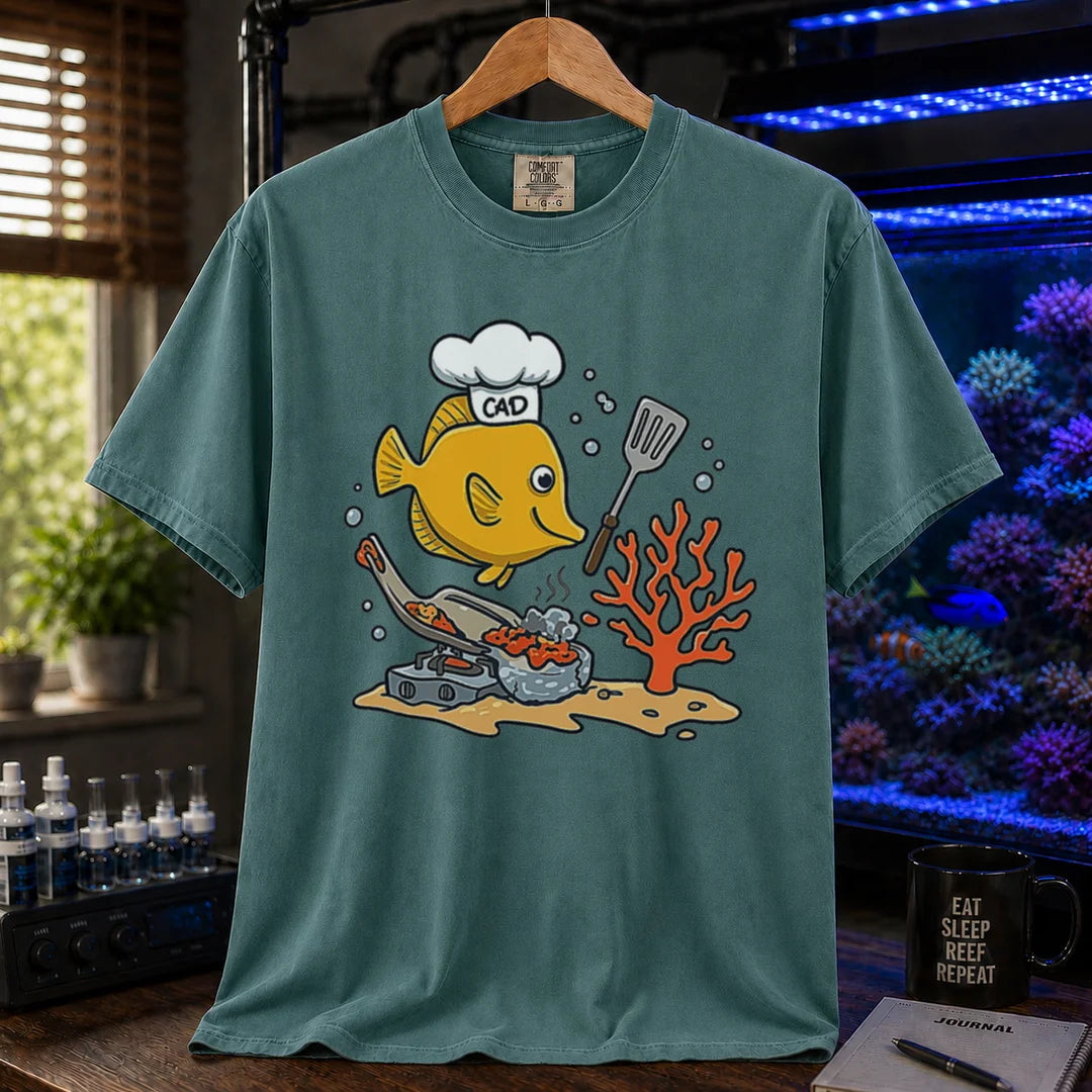 Saltwater aquarium graphic t-shirt featuring a yellow Tang wearing a chef hat and cooking with a spatula over a stove, green crew neck tee