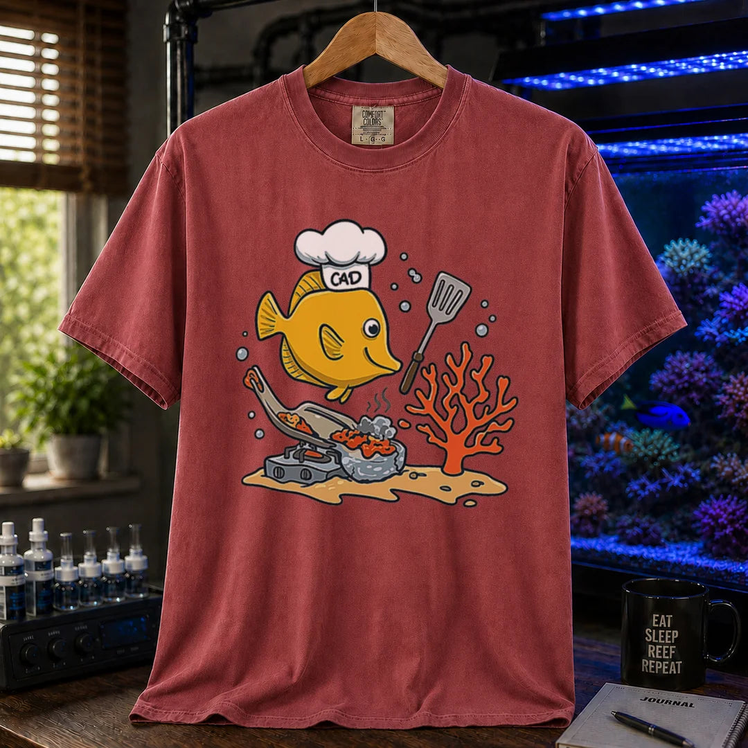 Saltwater aquarium graphic t-shirt featuring a yellow Tang wearing a chef hat and cooking with a spatula over a stove, maroon crew neck tee