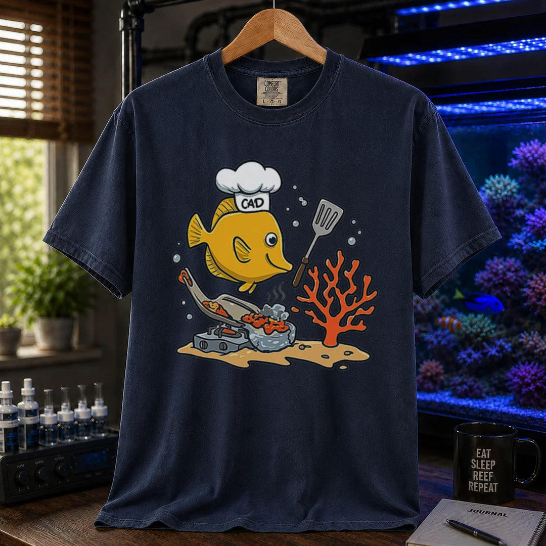 Saltwater aquarium graphic t-shirt featuring a yellow Tang wearing a chef hat and cooking with a spatula over a stove, navy crew neck tee