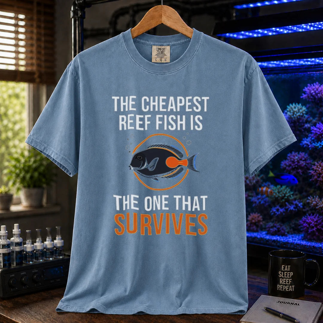 Saltwater aquarium graphic t-shirt featuring an Achilles Tang illustration inside a circular badge with text: THE CHEAPEST REEF FISH IS THE ONE THAT SURVIVES, blue crew neck tee