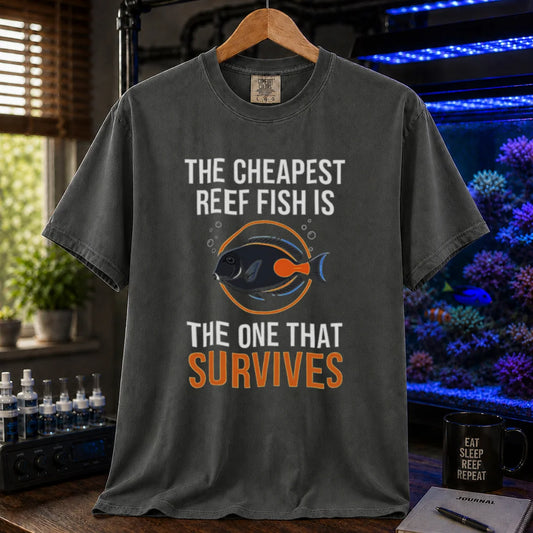 Saltwater aquarium graphic t-shirt featuring an Achilles Tang illustration inside a circular badge with text: THE CHEAPEST REEF FISH IS THE ONE THAT SURVIVES, khaki crew neck tee