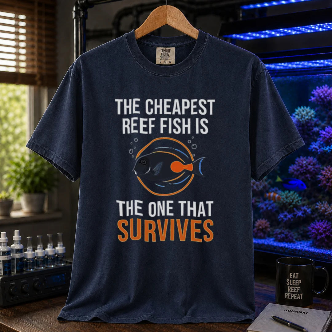 Saltwater aquarium graphic t-shirt featuring an Achilles Tang illustration inside a circular badge with text: THE CHEAPEST REEF FISH IS THE ONE THAT SURVIVES, navy crew neck tee