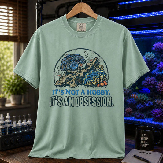Saltwater aquarium graphic t-shirt featuring a reef aquascape illustration and text: IT'S NOT A HOBBY. IT'S AN OBSESSION., green crew neck tee
