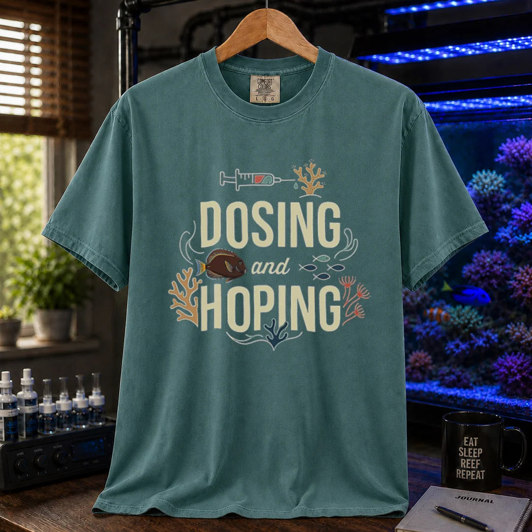 Saltwater aquarium graphic t-shirt featuring a dosing syringe and coral illustration with text: DOSING and HOPING, green crew neck tee