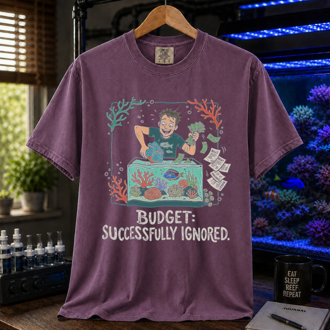 Saltwater aquarium graphic t-shirt featuring an aquarist tossing bills into a tank illustration with text: BUDGET: SUCCESSFULLY IGNORED., purple crew neck tee