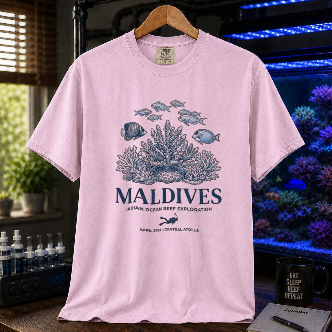 Saltwater aquarium graphic t-shirt featuring a coral reef and fish illustration with text: MALDIVES INDIAN OCEAN REEF EXPLORATION APRIL 2024 CENTRAL ATOLLS, pink crew neck tee