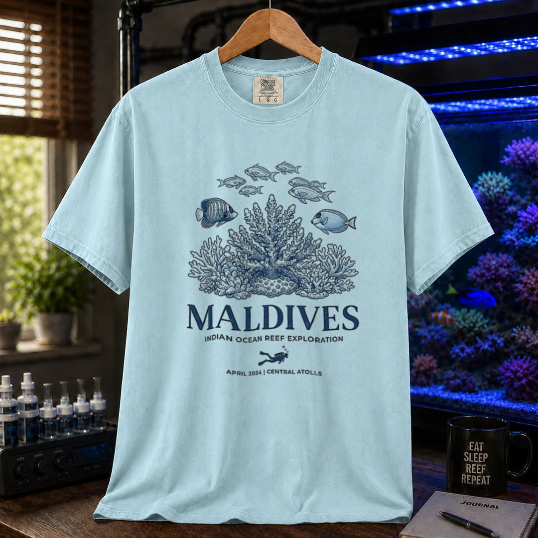Saltwater aquarium graphic t-shirt featuring a coral reef and fish illustration with text: MALDIVES INDIAN OCEAN REEF EXPLORATION APRIL 2024 CENTRAL ATOLLS, light blue crew neck tee