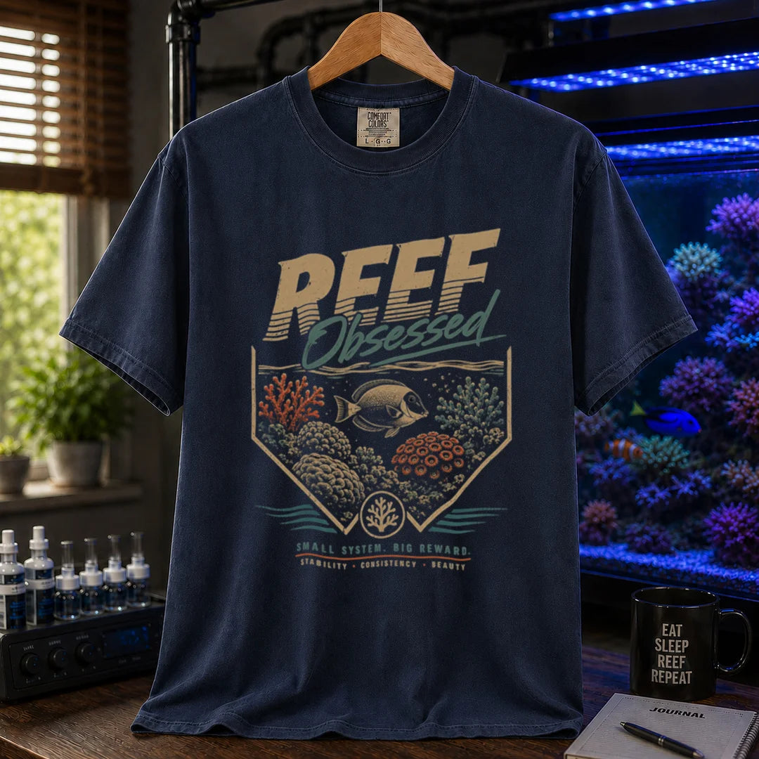 Saltwater aquarium graphic t-shirt featuring a retro coral emblem and text: REEF Obsessed SMALL SYSTEM. BIG REWARD. STABILITY . CONSISTENCY . BEAUTY, navy crew neck tee