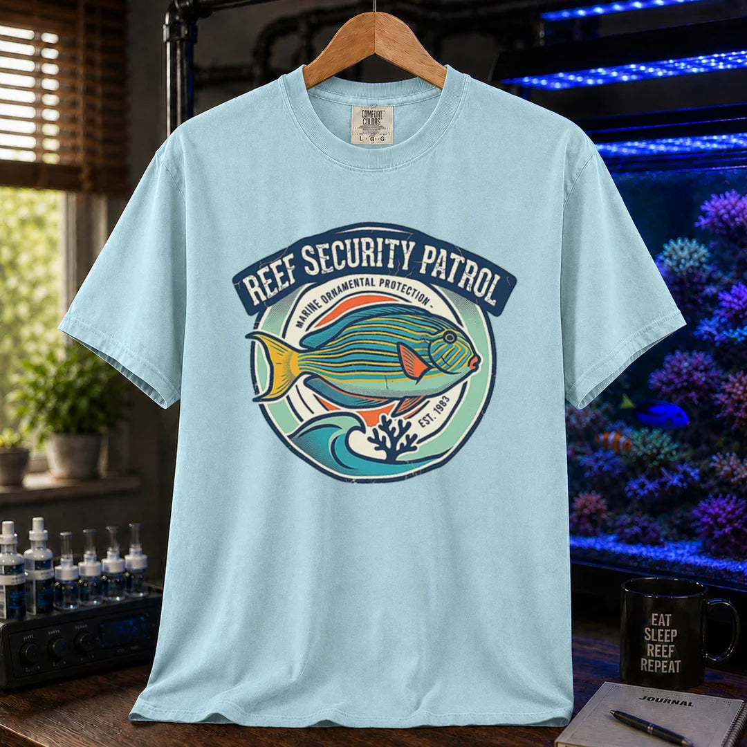 Saltwater aquarium graphic t-shirt featuring a circular emblem with a reef fish illustration and text: REEF SECURITY PATROL MARINE ORNAMENTAL PROTECTION EST. 1983, light blue crew neck tee