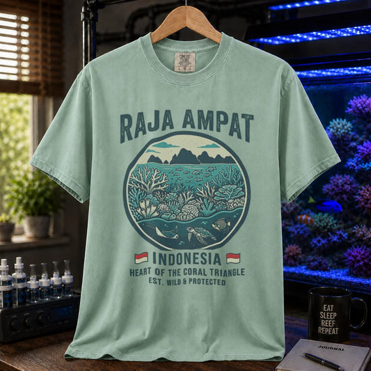 Saltwater aquarium graphic t-shirt featuring a circular reef landscape illustration and text: RAJA AMPAT INDONESIA HEART OF THE CORAL TRIANGLE EST. WILD & PROTECTED, green crew neck tee