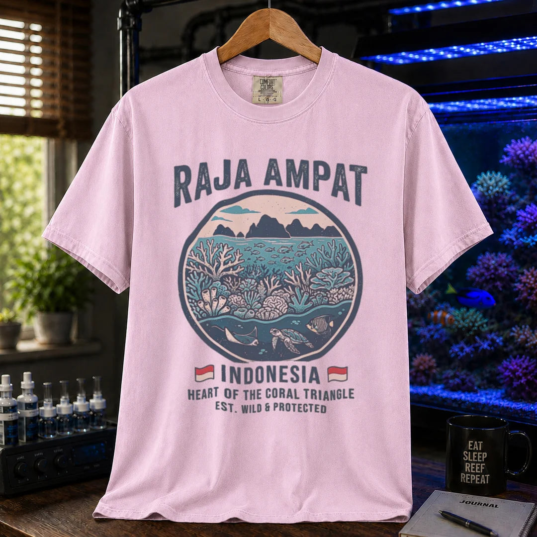 Saltwater aquarium graphic t-shirt featuring a circular reef landscape illustration and text: RAJA AMPAT INDONESIA HEART OF THE CORAL TRIANGLE EST. WILD & PROTECTED, pink crew neck tee