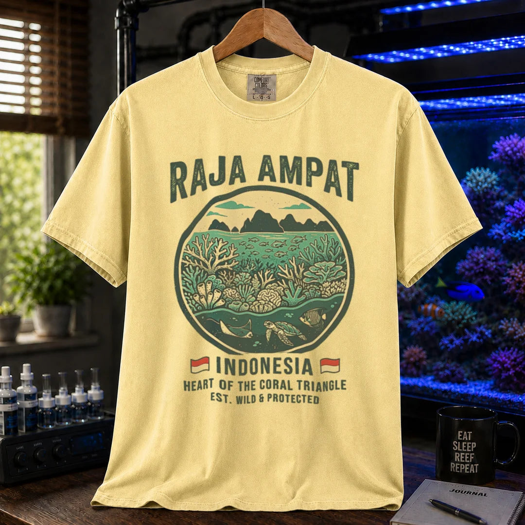 Saltwater aquarium graphic t-shirt featuring a circular reef landscape illustration and text: RAJA AMPAT INDONESIA HEART OF THE CORAL TRIANGLE EST. WILD & PROTECTED, yellow crew neck tee