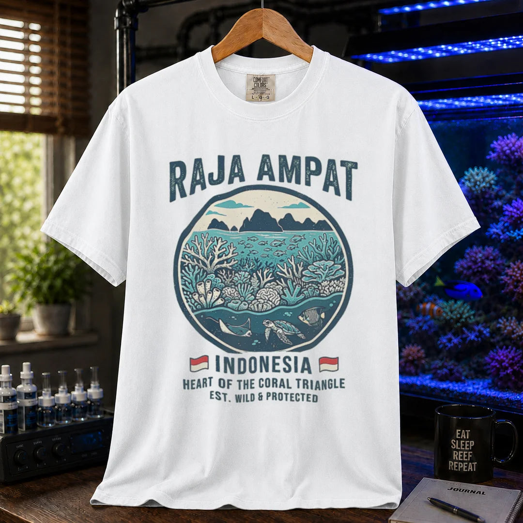 Saltwater aquarium graphic t-shirt featuring a circular reef landscape illustration and text: RAJA AMPAT INDONESIA HEART OF THE CORAL TRIANGLE EST. WILD & PROTECTED, white crew neck tee