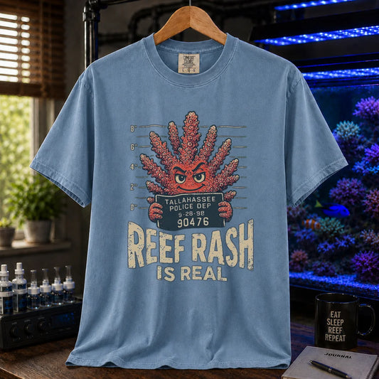 Saltwater aquarium graphic t-shirt featuring a mugshot of an anthropomorphic coral holding a police booking sign with text: REEF RASH IS REAL, blue crew neck tee