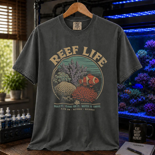 Saltwater aquarium graphic t-shirt featuring a circular reef landscape illustration with text: REEF LIFE BUILD IT. CARE FOR IT. WATCH IT THRIVE. PASSION . PATIENCE . BALANCE, dark grey crew neck tee