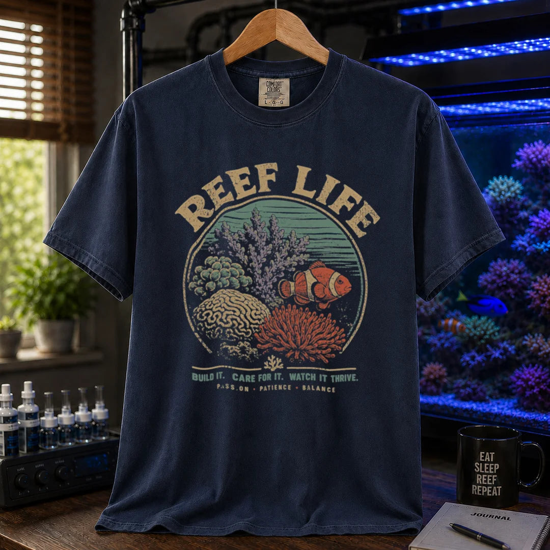 Saltwater aquarium graphic t-shirt featuring a circular reef landscape illustration with text: REEF LIFE BUILD IT. CARE FOR IT. WATCH IT THRIVE. PASSION . PATIENCE . BALANCE, navy crew neck tee
