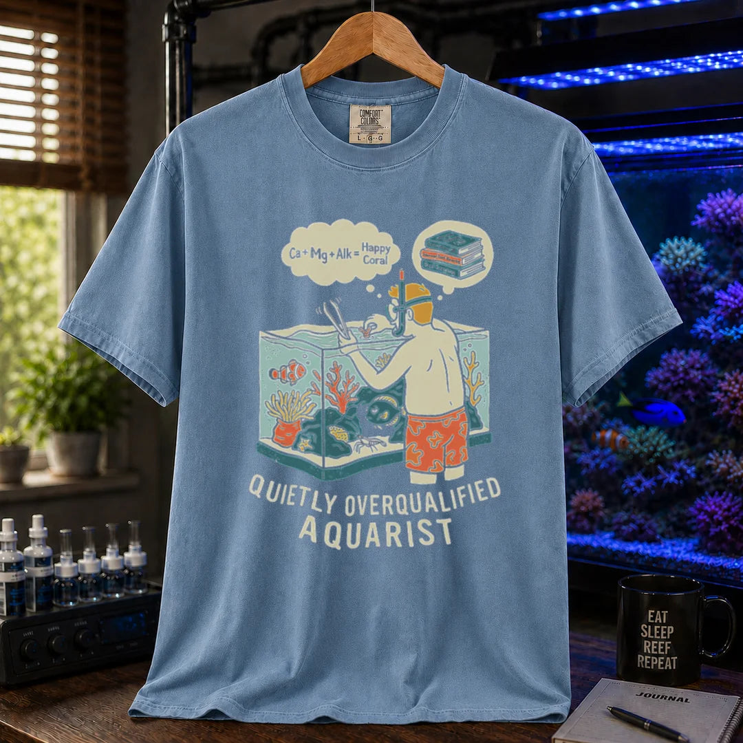 Saltwater aquarium graphic t-shirt featuring an aquarist maintaining a tank with chemical equation thought bubbles and text: QUIETLY OVERQUALIFIED AQUARIST, blue crew neck tee