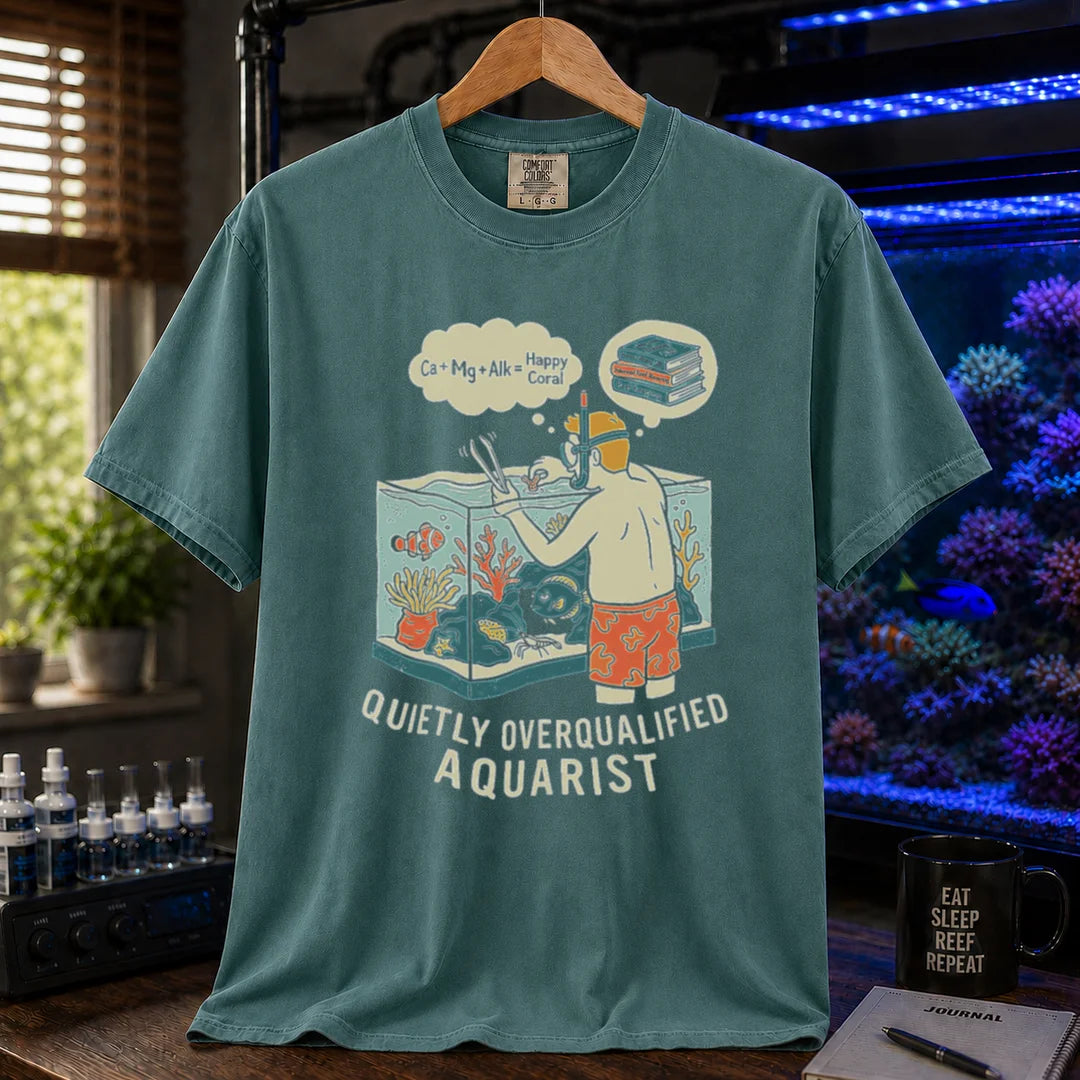 Saltwater aquarium graphic t-shirt featuring an aquarist maintaining a tank with chemical equation thought bubbles and text: QUIETLY OVERQUALIFIED AQUARIST, green crew neck tee