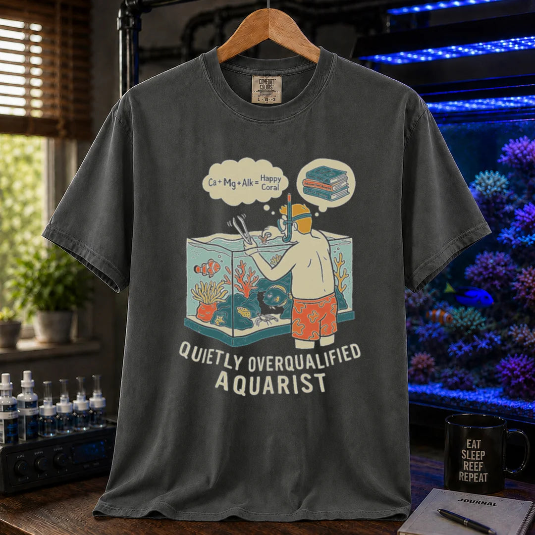 Saltwater aquarium graphic t-shirt featuring an aquarist maintaining a tank with chemical equation thought bubbles and text: QUIETLY OVERQUALIFIED AQUARIST, dark grey crew neck tee