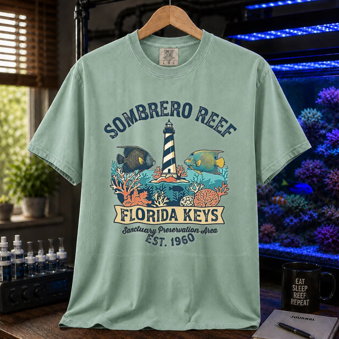 Saltwater aquarium graphic t-shirt featuring a lighthouse illustration, marine fish, and text: SOMBRERO REEF FLORIDA KEYS Sanctuary Preservation Area EST. 1960, green crew neck tee