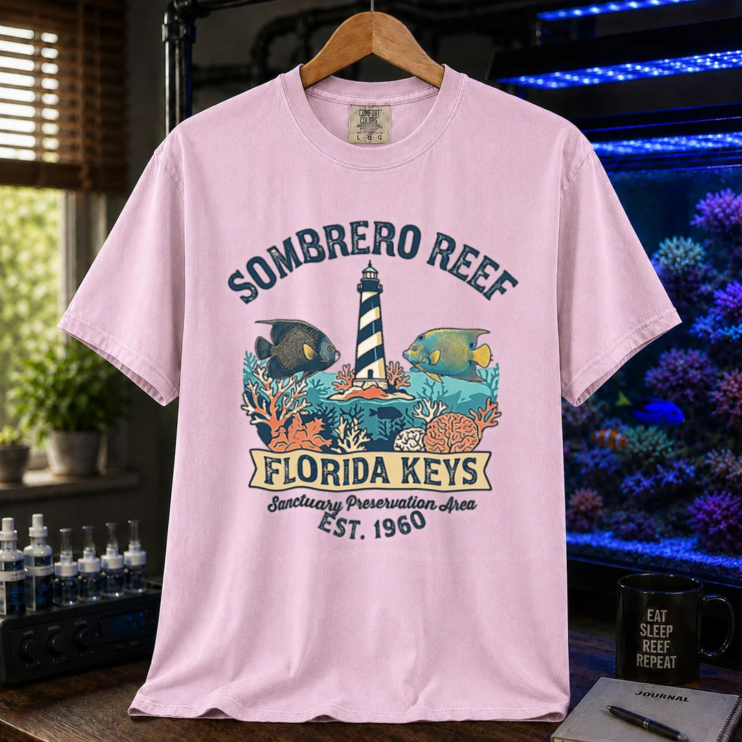 Saltwater aquarium graphic t-shirt featuring a lighthouse illustration, marine fish, and text: SOMBRERO REEF FLORIDA KEYS Sanctuary Preservation Area EST. 1960, pink crew neck tee