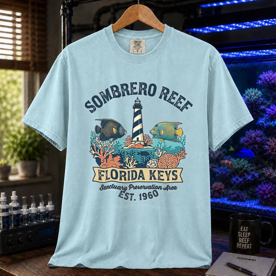 Saltwater aquarium graphic t-shirt featuring a lighthouse illustration, marine fish, and text: SOMBRERO REEF FLORIDA KEYS Sanctuary Preservation Area EST. 1960, light blue crew neck tee