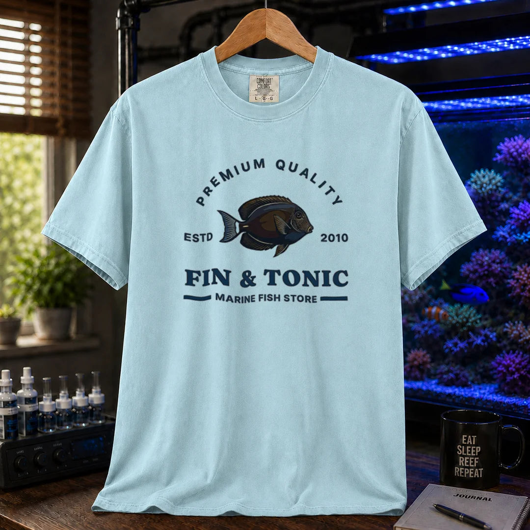 Saltwater aquarium graphic t-shirt featuring a marine fish badge design and text: PREMIUM QUALITY ESTD 2010 FIN & TONIC MARINE FISH STORE, light blue crew neck tee