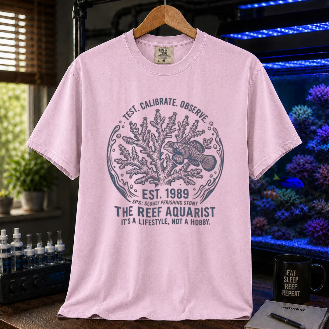 Saltwater aquarium graphic t-shirt featuring a circular coral and fish badge with text: TEST. CALIBRATE. OBSERVE. EST. 1989 THE REEF AQUARIST IT'S A LIFESTYLE, NOT A HOBBY., pink crew neck tee