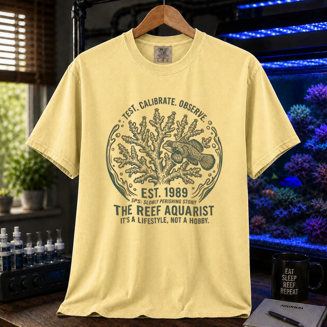 Saltwater aquarium graphic t-shirt featuring a circular coral and fish badge with text: TEST. CALIBRATE. OBSERVE. EST. 1989 THE REEF AQUARIST IT'S A LIFESTYLE, NOT A HOBBY., yellow crew neck tee