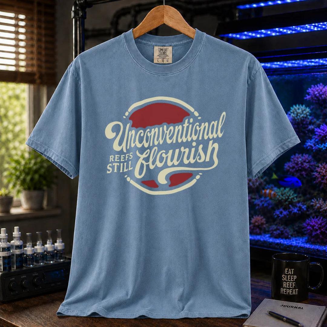 Saltwater aquarium graphic t-shirt featuring a retro red and blue badge with cream typography reading Unconventional Reefs Still Flourish, blue crew neck tee