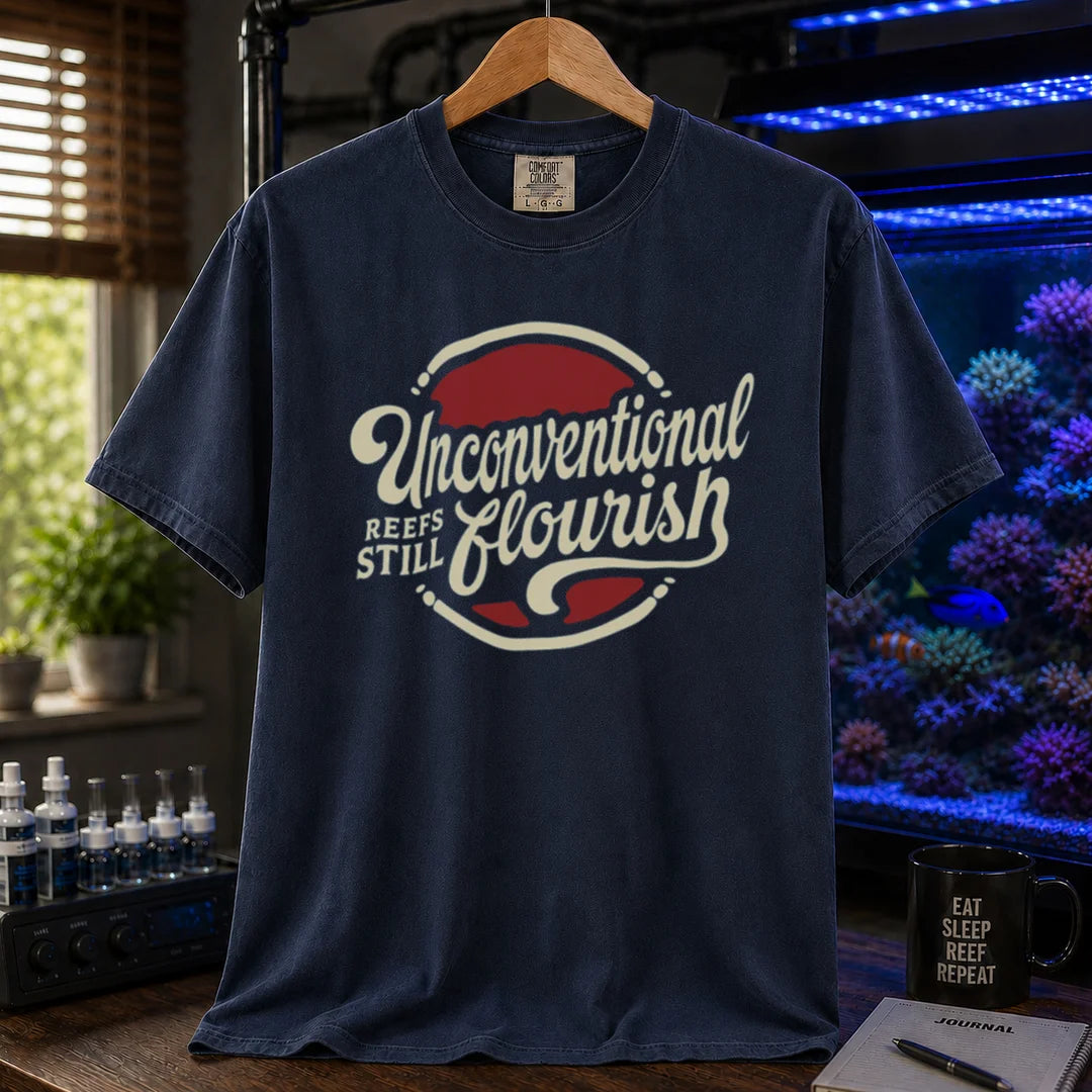 Saltwater aquarium graphic t-shirt featuring a retro red and blue badge with cream typography reading Unconventional Reefs Still Flourish, navy crew neck tee