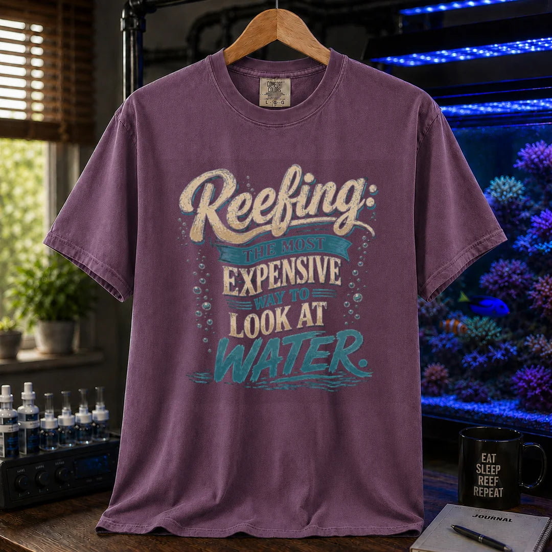Saltwater aquarium graphic t-shirt featuring cream and blue typography reading Reefing: The Most Expensive Way To Look At Water with bubble accents, purple crew neck tee