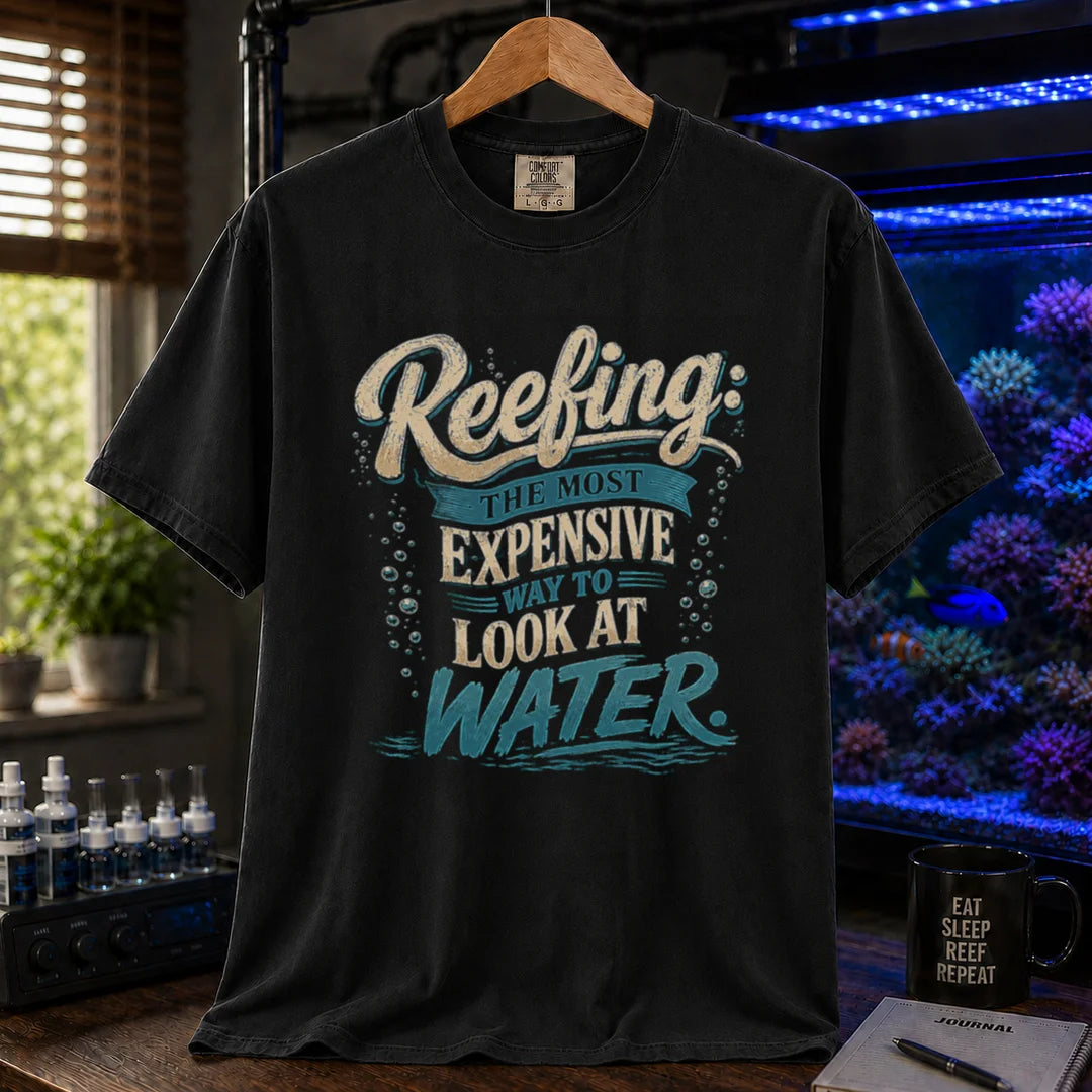 Saltwater aquarium graphic t-shirt featuring cream and blue typography reading Reefing: The Most Expensive Way To Look At Water with bubble accents, black crew neck tee