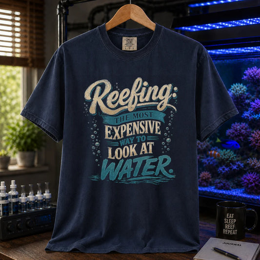 Saltwater aquarium graphic t-shirt featuring cream and blue typography reading Reefing: The Most Expensive Way To Look At Water with bubble accents, navy crew neck tee