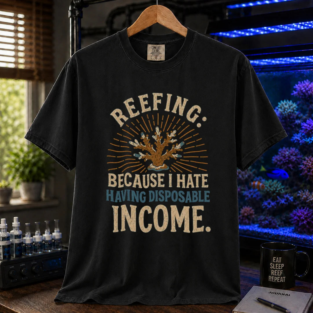 Saltwater aquarium graphic t-shirt featuring distressed cream and blue typography reading Reefing: Because I Hate Having Disposable Income with a coral illustration and sunburst background, black crew neck tee