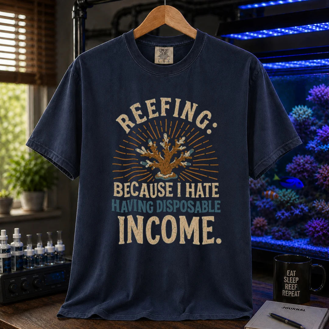 Saltwater aquarium graphic t-shirt featuring distressed cream and blue typography reading Reefing: Because I Hate Having Disposable Income with a coral illustration and sunburst background, navy crew neck tee