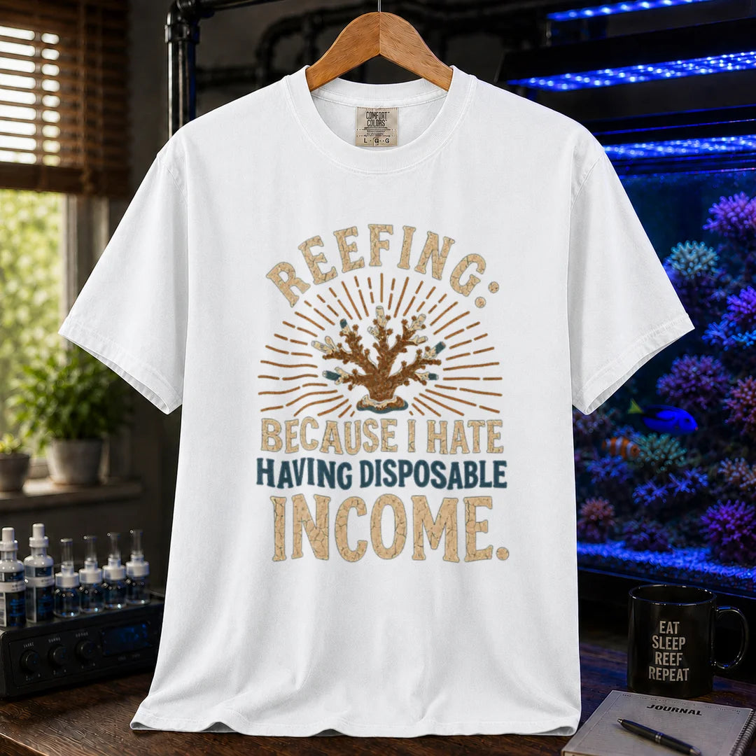 Saltwater aquarium graphic t-shirt featuring distressed cream and blue typography reading Reefing: Because I Hate Having Disposable Income with a coral illustration and sunburst background, white crew neck tee