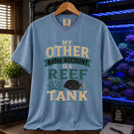 Saltwater aquarium graphic t-shirt featuring cream and teal distressed typography reading My Other Bank Account Is A Reef Tank with coral and tang illustrations, blue crew neck tee