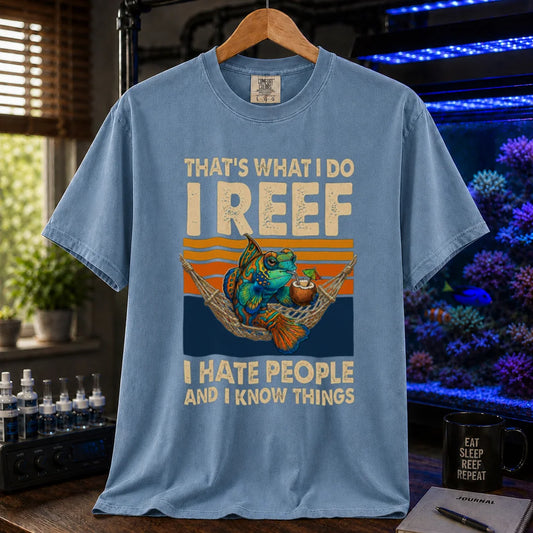 Saltwater aquarium graphic t-shirt featuring a mandarin goby in a hammock with a drink against a retro sunset and text reading That's What I Do I Reef I Hate People And I Know Things, blue crew neck tee