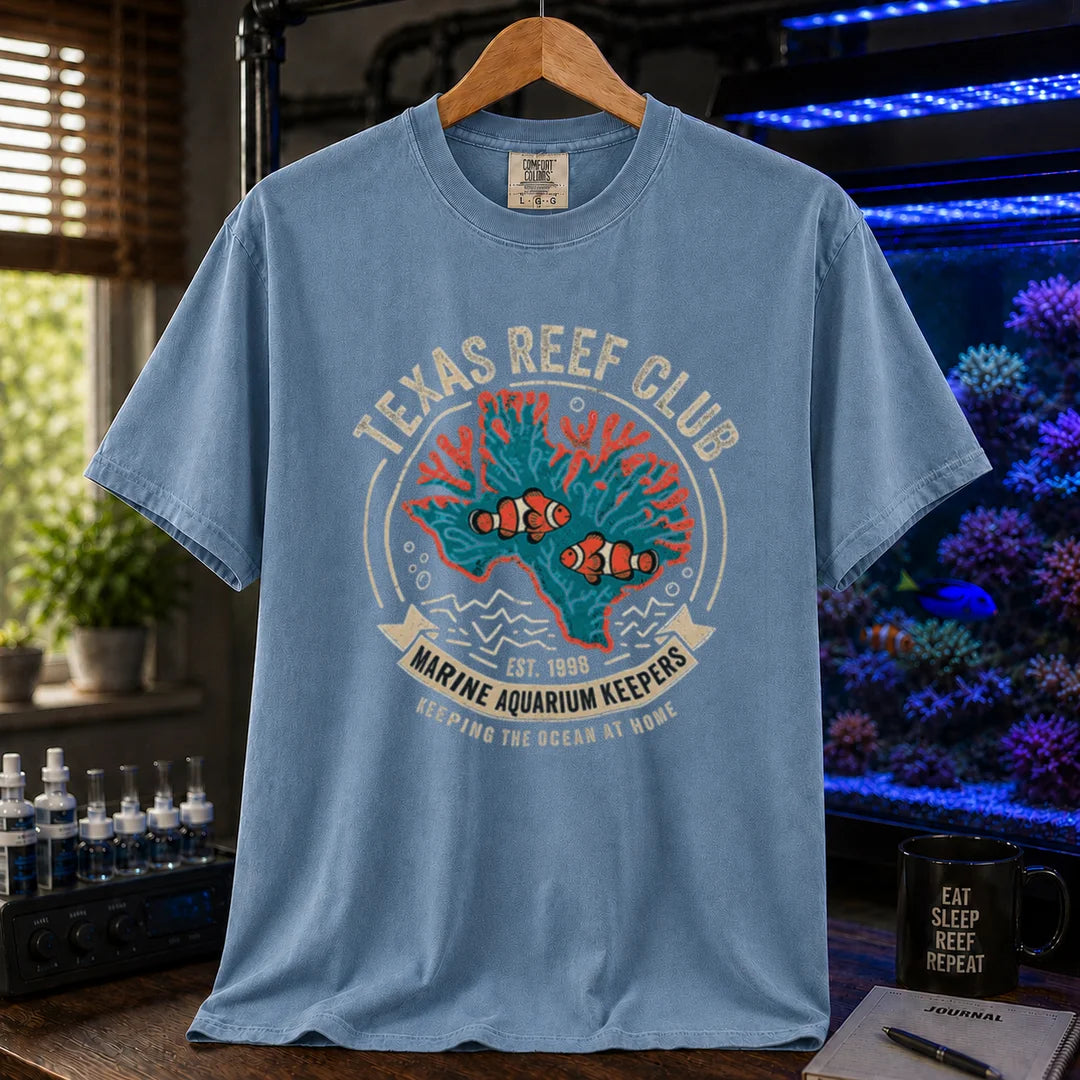 Saltwater aquarium graphic t-shirt featuring a vintage emblem with coral shaped like Texas, clownfish, and text reading Texas Reef Club Marine Aquarium Keepers Est. 1998, blue crew neck tee