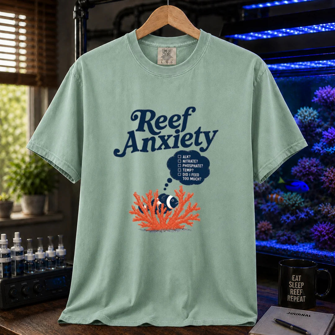 Saltwater aquarium graphic t-shirt featuring blue text reading Reef Anxiety and an illustration of a clownfish in coral with a thought bubble checklist, green crew neck tee