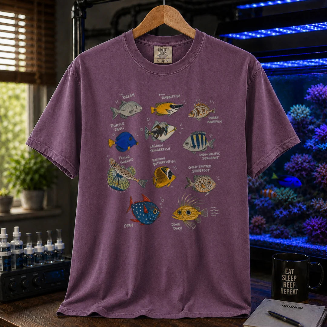 Saltwater aquarium graphic t-shirt design featuring a vintage marine species field guide layout with labeled illustrations of various fish including a Purple Tang, Lagoon Triggerfish, and Flying Gurnard, purple crew neck tee